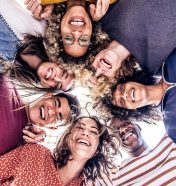 Multicultural group of young people standing in circle and smiling at camera - Happy diverse friends having fun hugging together - Low angle view