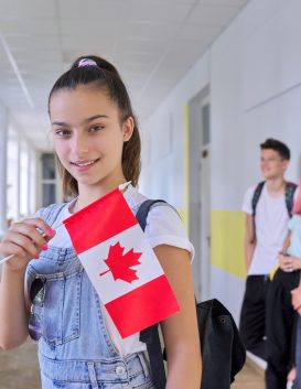 Student teenager female with flag of Canada inside school, children group background. Canada, education and youth, patriotism, people concept